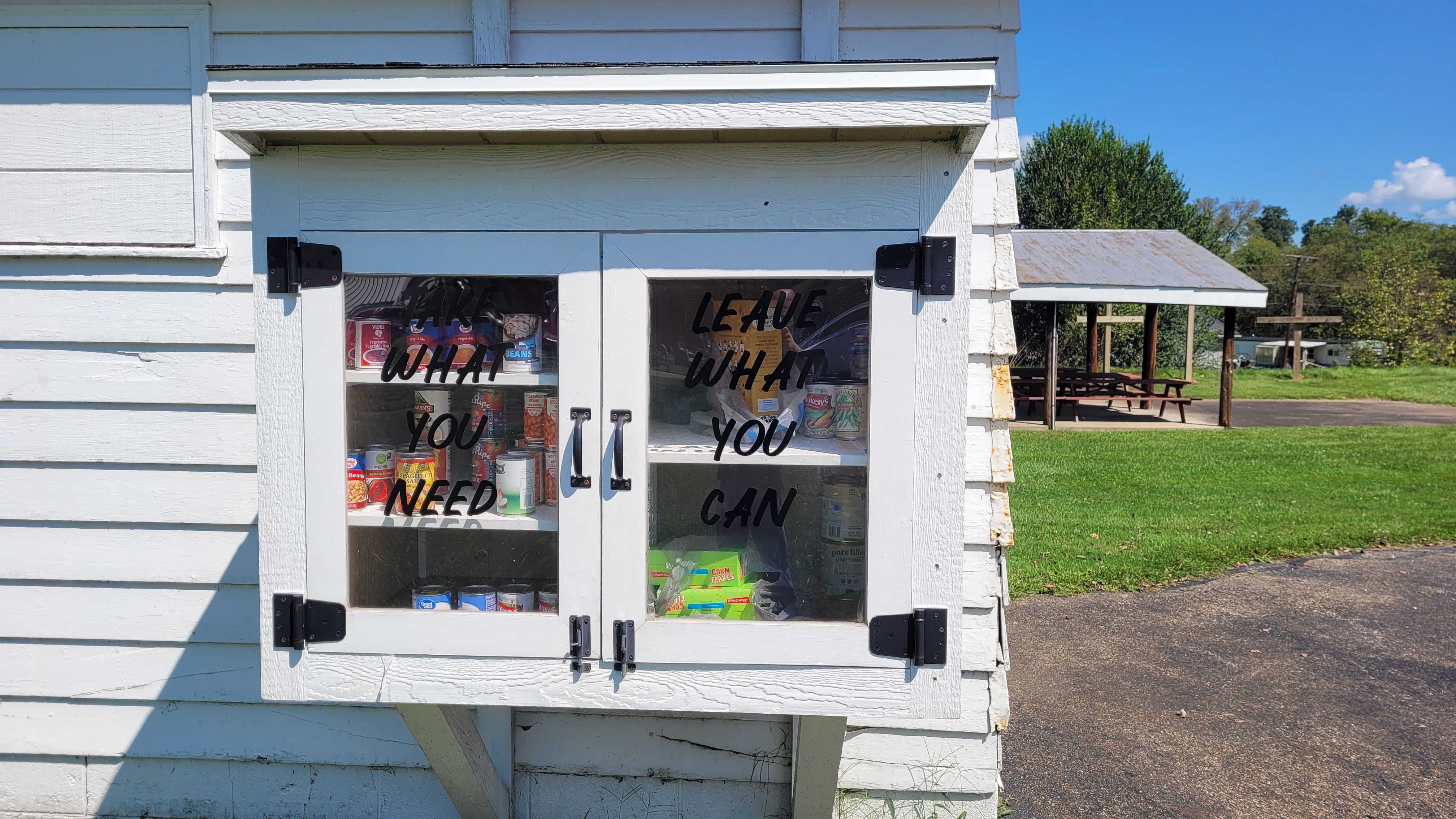 The church's Blessing Box, a white cabinet mounted on the building and stocked with canned goods, lettered 'Take what you need, leave what you can'.