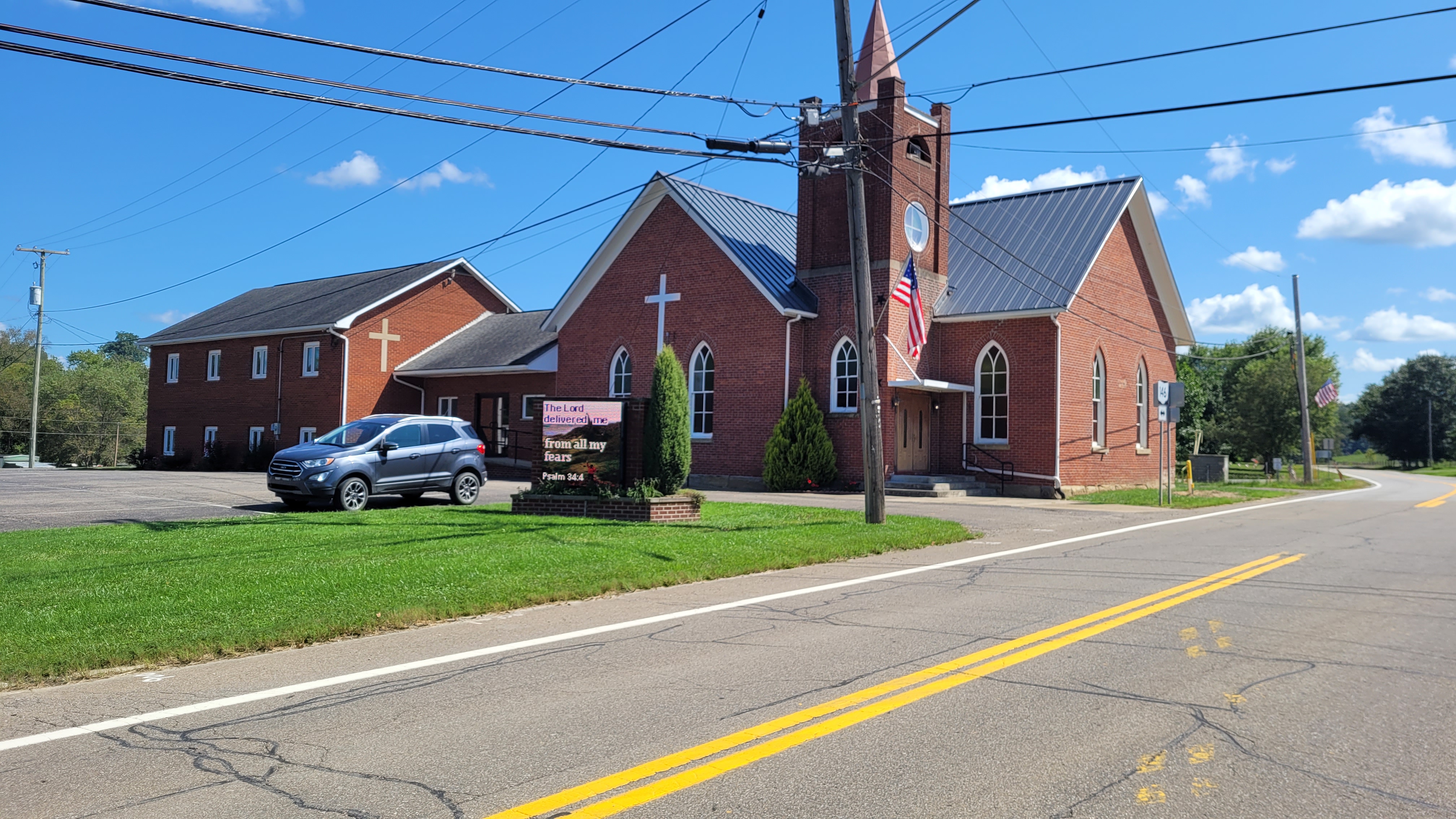The brick sanctuary of Chandlersville Methodist Church with its steeple, seen from Chandlersville Road on a clear day.