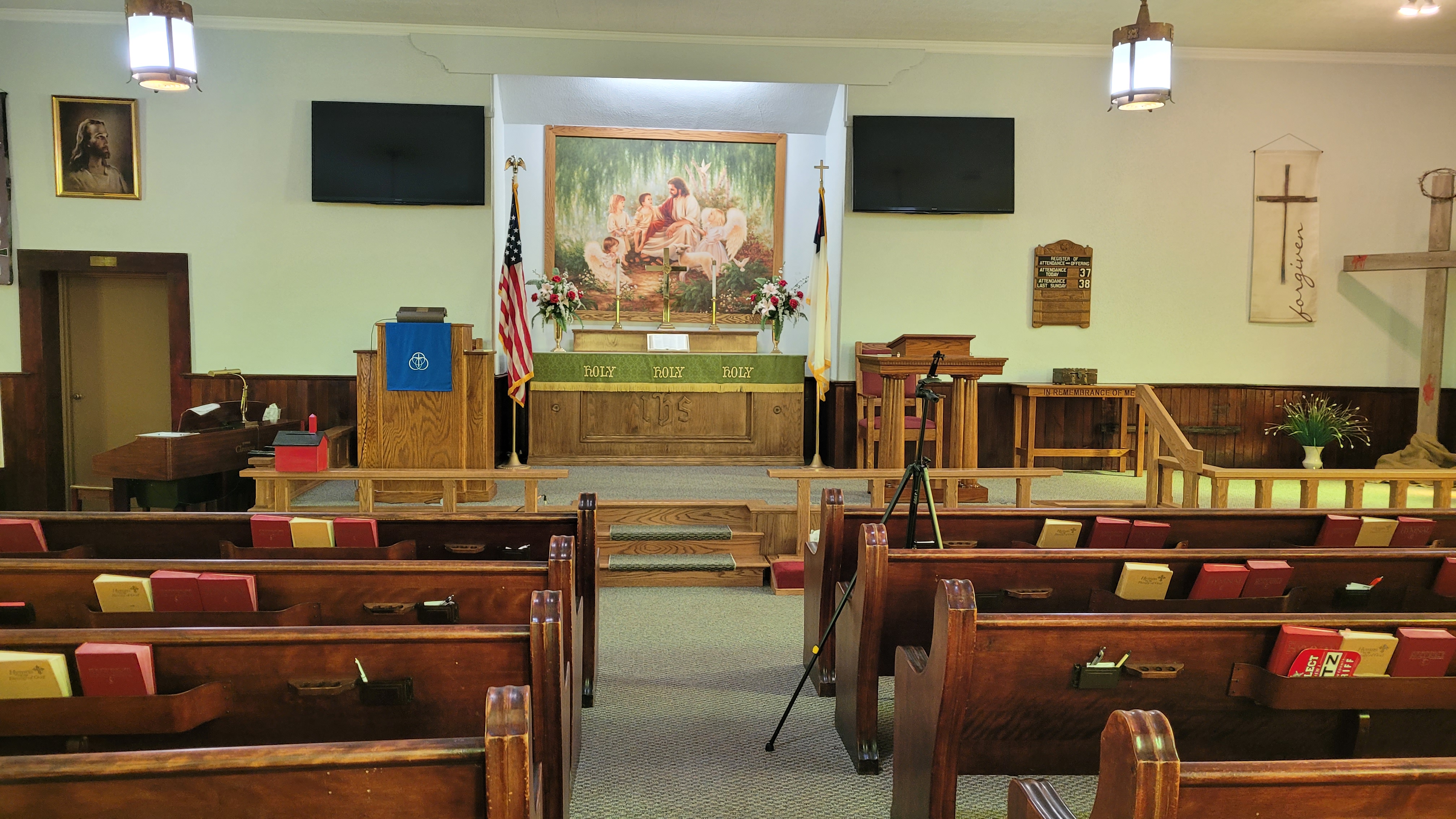The sanctuary looking toward the altar, with a painting of Jesus, flowers, candles, and a green altar cloth reading Holy, Holy, Holy.