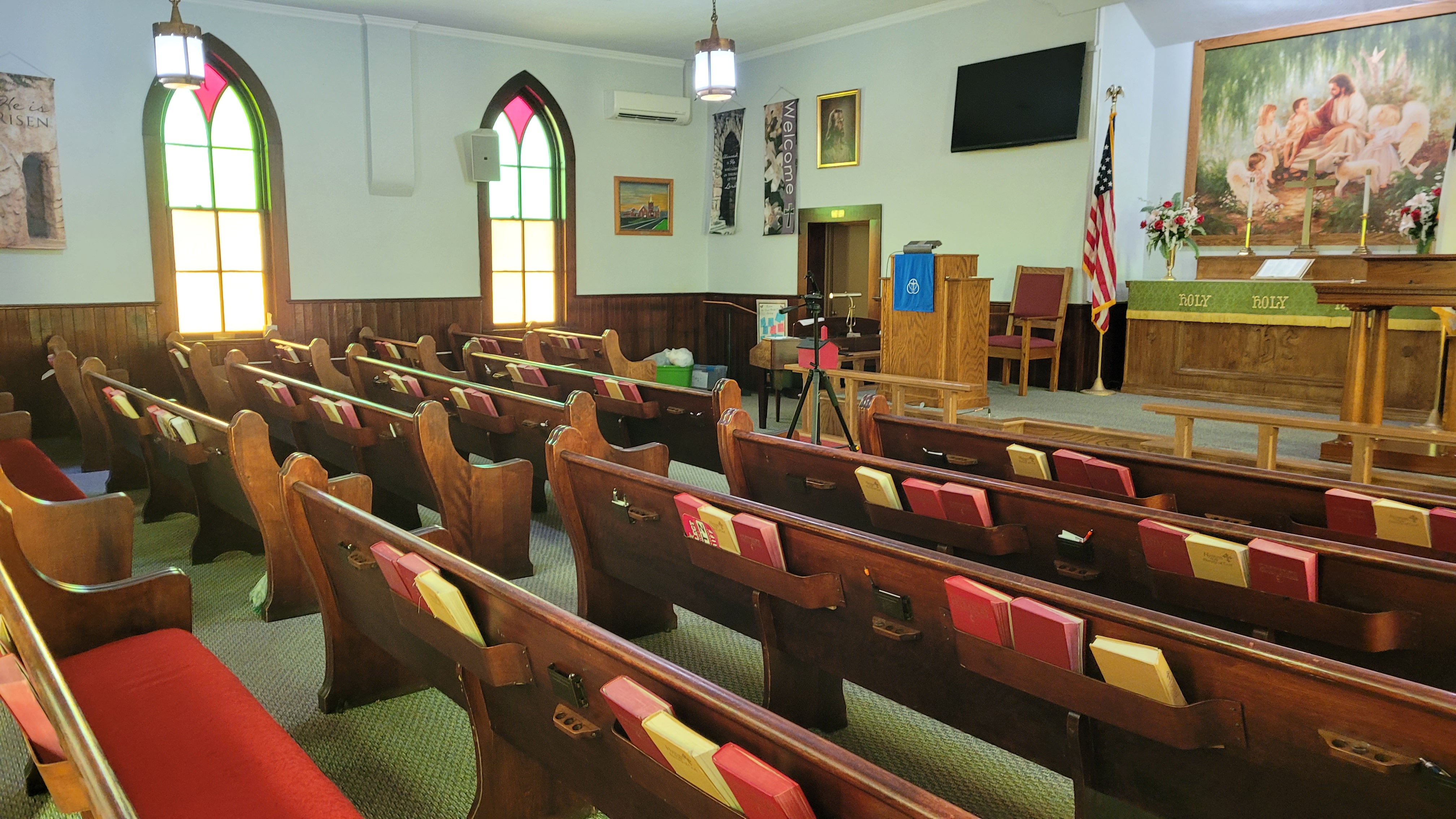 The sanctuary seen from the front, with rows of wooden pews, hymnals in the racks, and arched stained glass windows along the wall.